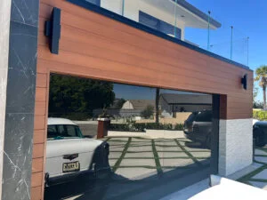 Contemporary house exterior featuring a sleek reflective glass garage door framed with warm wood panels for a stylish modern look.