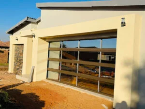 Contemporary beige home featuring a stylish glass-panel garage door that adds elegance, visibility, and modern curb appeal.