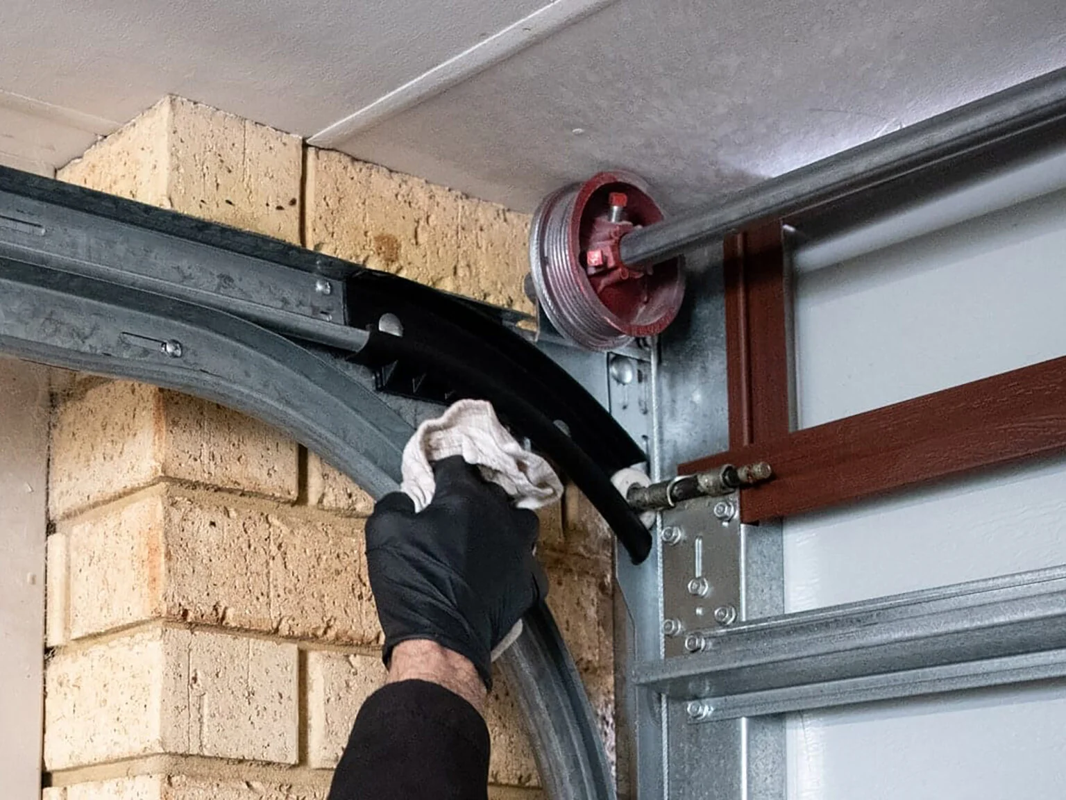 Technician cleaning the upper arch and spring of a residential garage door to ensure smooth and safe operation.