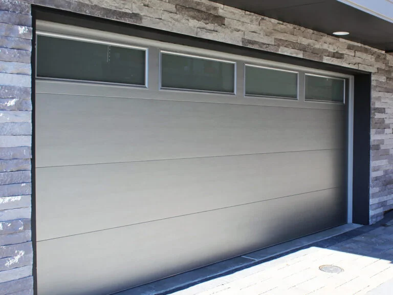 Light gray sectional garage door with horizontal panels and narrow glass transoms at top.