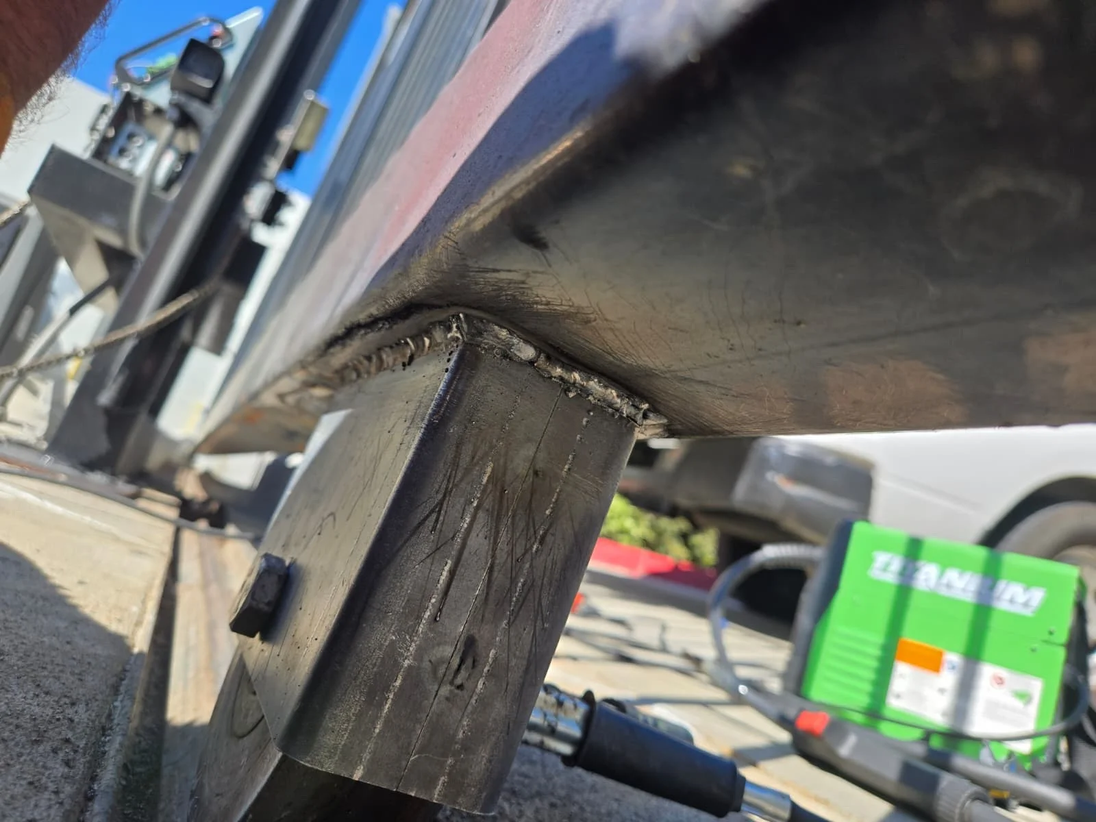 Close-up view of welded sliding gate bottom track and roller assembly during gate repair and alignment work.